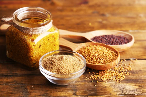 Mustard seeds, powder and sauce in glass jar, bowl and wooden spoons on wooden background — Stock Photo, Image