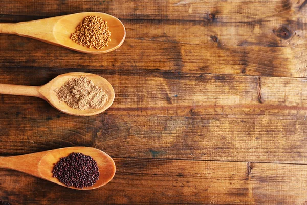 Семена горчицы, порошок и соус в деревянных ложках на деревянном фоне — стоковое фото