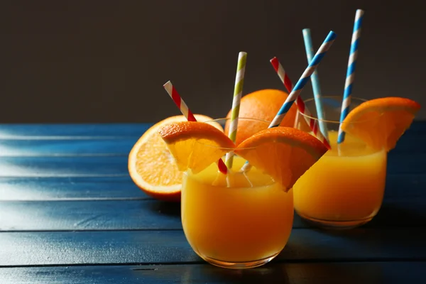 Vaso de zumo de naranja con pajitas y rodajas sobre mesa de madera de color, sobre fondo oscuro — Foto de Stock