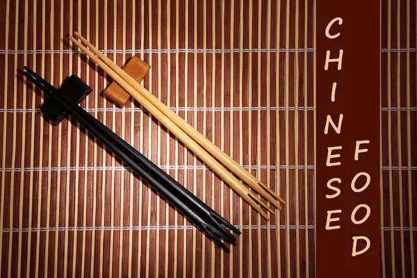 Par de palillos y texto de comida china sobre fondo de estera de bambú marrón —  Fotos de Stock