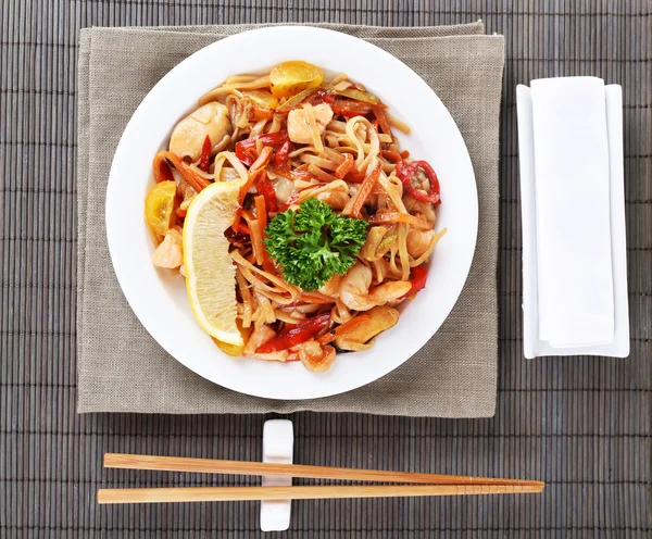 Macarrão chinês com legumes e frutos do mar na placa no fundo tapete de bambu — Fotografia de Stock