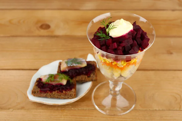 Insalata di aringhe russe in ciotola di vetro e panini con aringhe salate, su sfondo tavolo di legno — Foto Stock