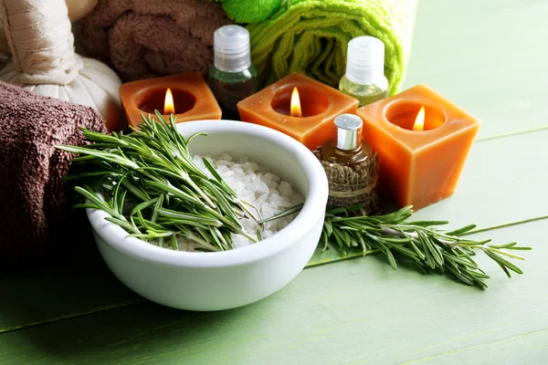Branches of rosemary and sea salt in bowl, towels, candles and bottle with massage oil on wooden background. Rosemary spa concept — Stock Photo, Image