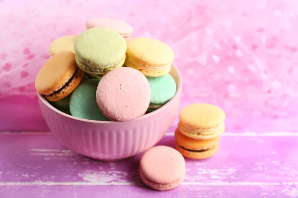Assortment of gentle colorful macaroons in colorful mug on color wooden table, on light background — Stock Photo, Image