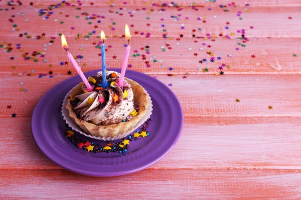 Torta tazza di compleanno con candele con scintille sul piatto su sfondo del tavolo in legno a colori — Foto Stock