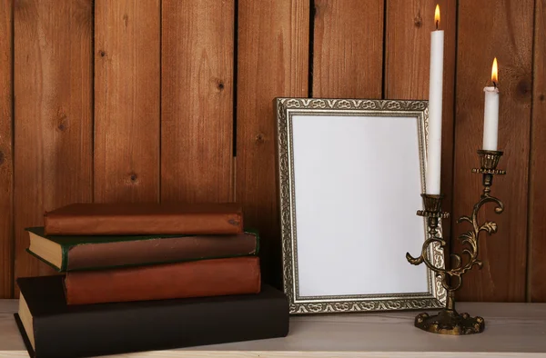 Moldura com velas e livros sobre superfície de madeira e fundo de parede de madeira — Fotografia de Stock