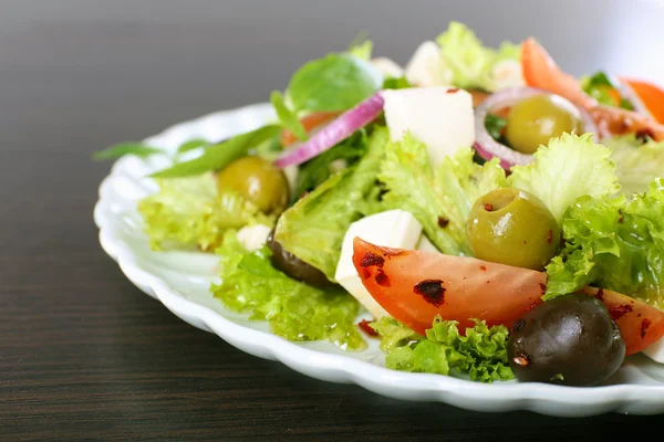 Griekse salade in plaat op houten ondergrond — Stockfoto