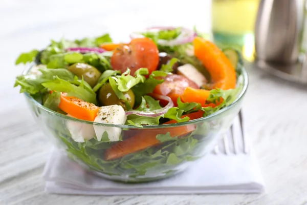 Greek salad in glass dish on napkin and color wooden background — Stock Photo, Image