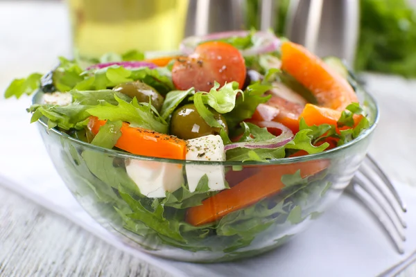 Греческий салат в стеклянной тарелке на салфетке и цветном деревянном фоне — стоковое фото