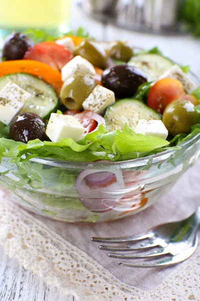 Greek salad in glass dish with fork on napkin and wooden table background — Stock Photo, Image