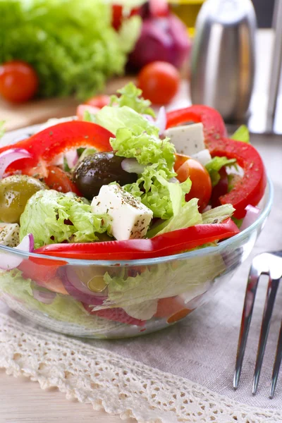 Griechischer Salat in Glasschale mit Gabel und Gemüsehintergrund — Stockfoto