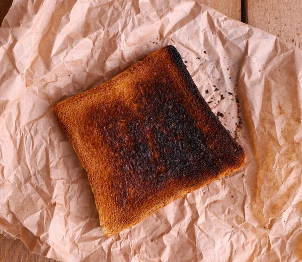 Pane tostato bruciato su un pezzo di carta e sfondo tavolo di legno — Foto Stock