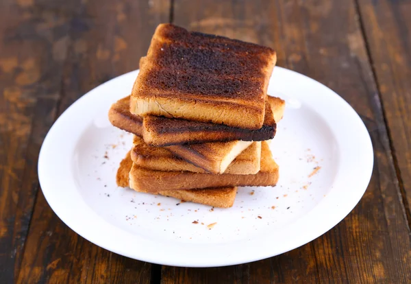 Verbrande toast brood op plaat, op houten tafel achtergrond — Stockfoto