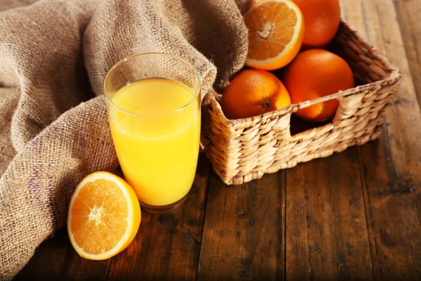 Kieliszek soku pomarańczowego z plastrami i Wiklinowy kosz płótnie szmatką na drewnianym stole tło — Zdjęcie stockowe