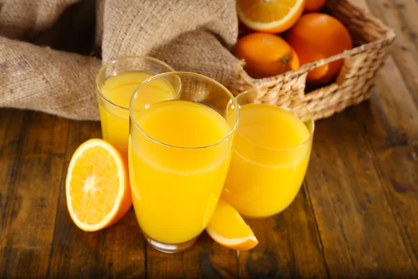 Vaso de zumo de naranja con rodajas y cesta de mimbre con tela de arpillera sobre fondo de mesa de madera —  Fotos de Stock