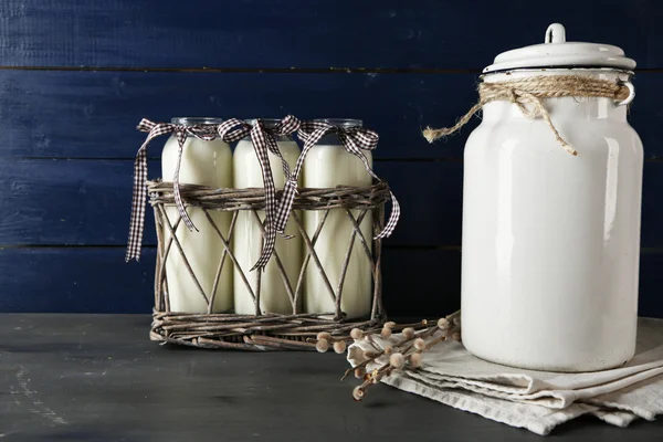 Milk can and glass bottles on color wooden background — Stock Photo, Image