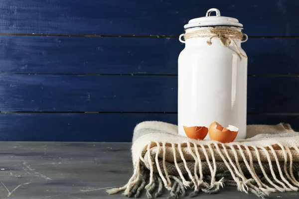 Milk can with eggshell on color wooden background