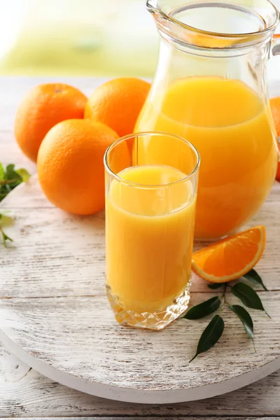 Glass of orange juice and oranges on color wooden table background — Stock Photo, Image