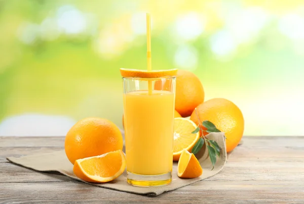Glas sinaasappelsap met stro en segmenten op houten tafel en lichte achtergrond — Stockfoto