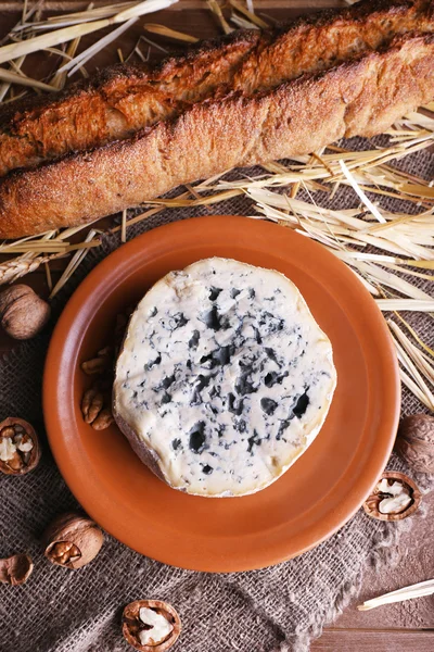 Queijo azul em prato de barro com nozes, baguete e feno em pano de serapilheira e fundo de mesa de madeira — Fotografia de Stock
