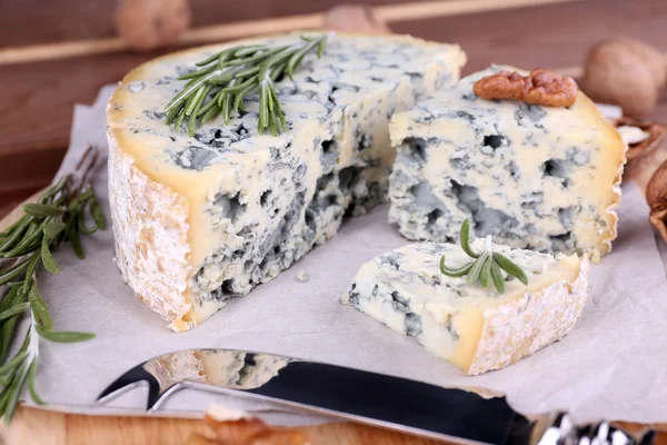 Blue cheese with sprigs of rosemary and nuts on board with knife and wooden table background — Stock Photo, Image