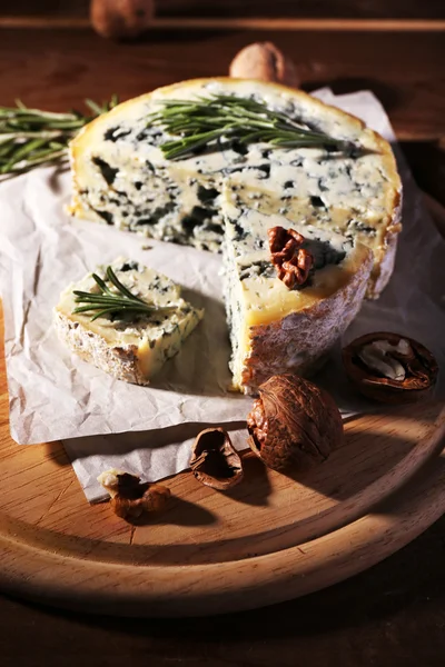 Formaggio blu con rametti di rosmarino e noci a bordo con foglio di carta e fondo tavola in legno — Foto Stock