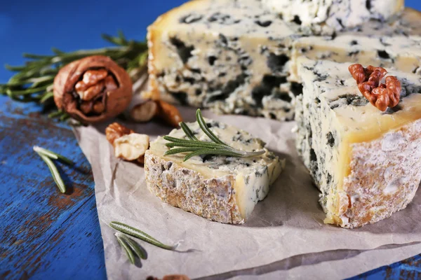 Μπλε τυρί με κλωναράκια δεντρολίβανο και ξηρών καρπών σε φύλλο χαρτιού και το χρώμα φόντου ξύλινο τραπέζι — Φωτογραφία Αρχείου
