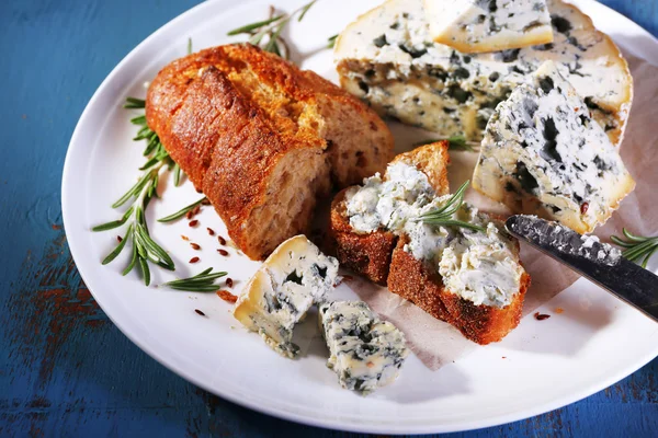 Blue cheese with sprigs of rosemary, bread and nuts on plate and color wooden table background — Stock Photo, Image