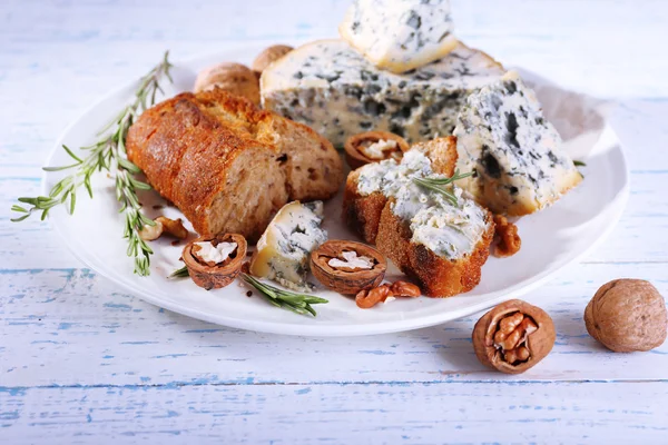 Blue cheese with sprigs of rosemary, bread and nuts on plate and color wooden table background — Stock Photo, Image