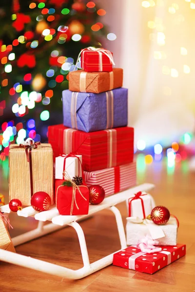 Present boxes on sledge on wooden floor near Christmas tree, indoors — Stock Photo, Image