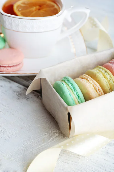 Bunte Makronen mit Tasse Tee auf farbigem Holzhintergrund — Stockfoto