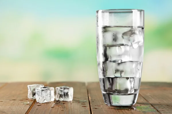 Glass of water with ice on wooden table and light blurred background — Stock Photo, Image