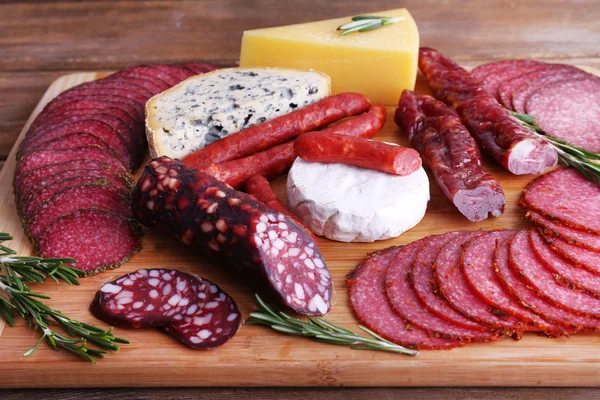 Surtido de embutidos ahumados y queso sobre tabla de cortar y fondo de mesa de madera —  Fotos de Stock