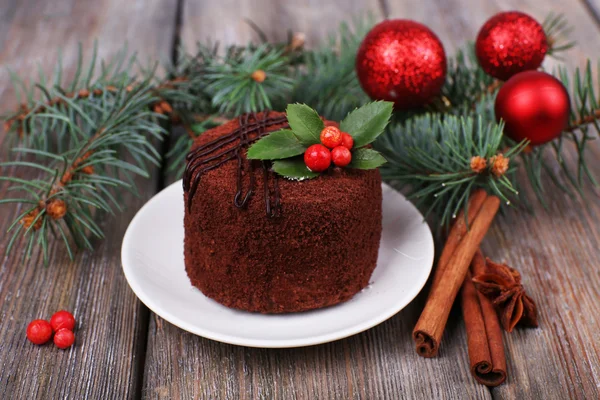 Delicioso pastel de chocolate en platillo con acebo y bayas en la decoración de Navidad y fondo de madera —  Fotos de Stock