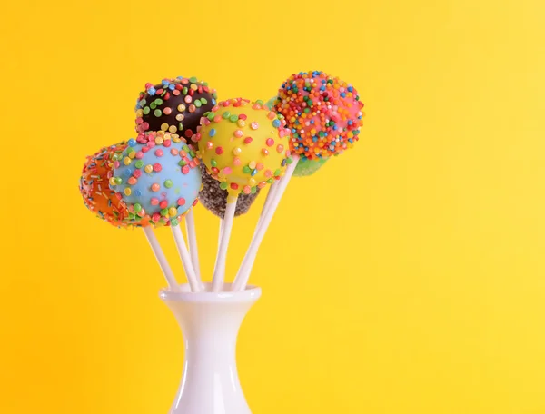 Sweet cake pops in vase on yellow background — Stock Photo, Image