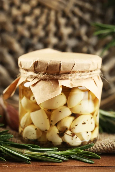 Ingeblikte knoflook in glazen pot en rieten mat en rozemarijn takken, op houten achtergrond — Stockfoto