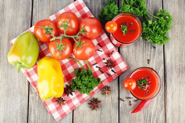 Tomatensap in glazen en verse groenten op servet op houten achtergrond — Stockfoto
