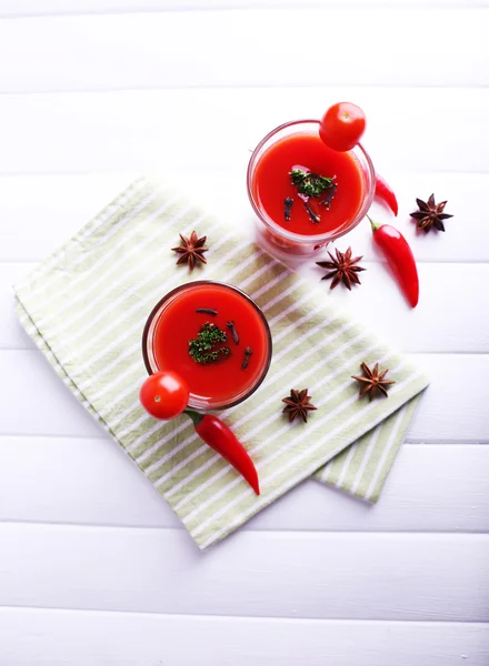 Tomato juice in glasses and fresh vegetables on napkin on light wooden background — Stock Photo, Image