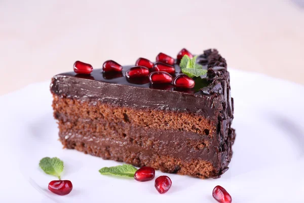 Deliziosa torta al cioccolato decorata con semi di melograno sul piatto sul tavolo — Foto Stock