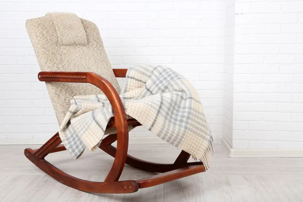 Rocking chair bedekt met plaid op houten vloer in de buurt van de bakstenen muur achtergrond — Stockfoto