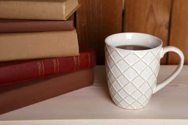 Bücherstapel mit Tasse auf Tischplatte und Holzhintergrund — Stockfoto