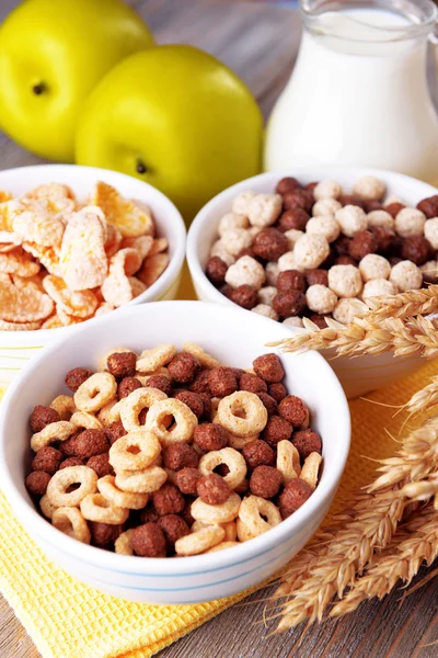 Diverses céréales sucrées dans un bol en céramique, fruits et cruche avec du lait sur la serviette, sur fond en bois de couleur — Photo