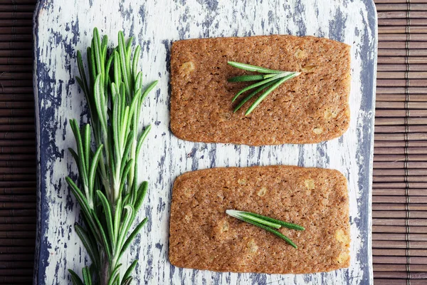 Knäckebröd met takjes rozemarijn op houten snijplank op bamboe mat achtergrond — Stockfoto