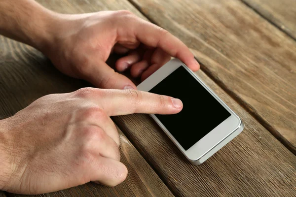 Manos sosteniendo el teléfono móvil inteligente sobre fondo de mesa de madera — Foto de Stock