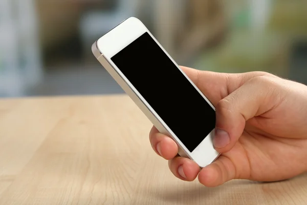 木製のテーブルと光のスマートな携帯電話を持っている手がぼやけて背景 — ストック写真