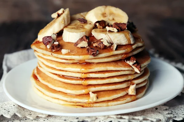 チョコレート、蜂蜜、ナッツ、皿にバナナと木製の背景にナプキンのスライスとおいしいパンケーキのスタック — ストック写真