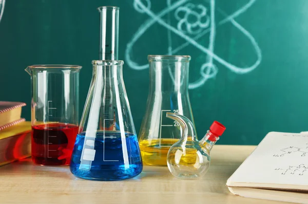 Desk in chemistry class with test tubes on green blackboard background — Stock Photo, Image