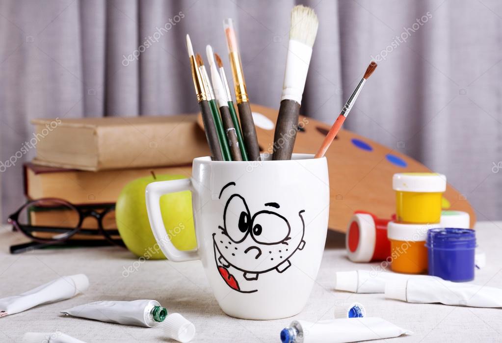 Emotional cup with brushes and paints on wooden table