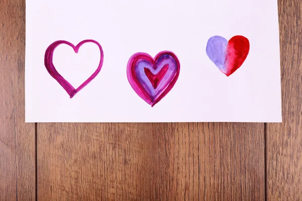 Painted hearts shape on sheet of paper on wooden table background — Stock Photo, Image