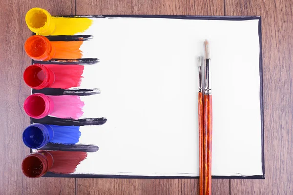 Bunte Farbstriche mit Pinsel und Farbdosen auf weißem Blatt Papier auf hölzernem Tischhintergrund — Stockfoto